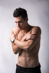 Shirtless young man hugging himself
