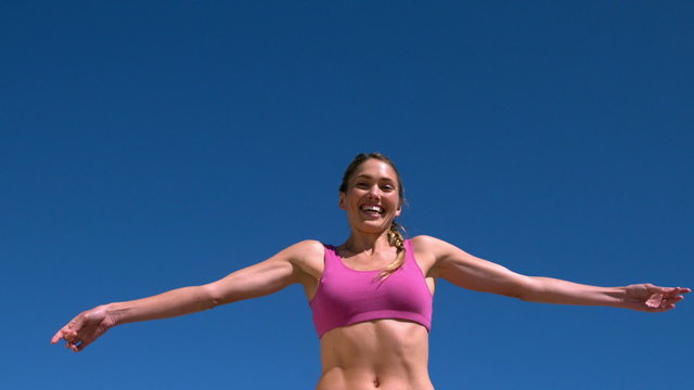 Fit blonde smiling and jumping up on sunny day