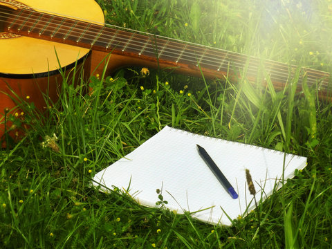 Photo guitar and notepad with pen on the grass