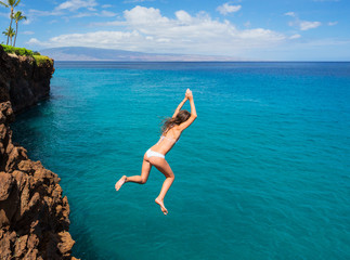 Woman jumping off cliff into the ocean