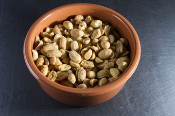 Dry roasted peanuts in terracotta  ramekin on slate.