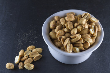 Dry roasted peanuts in white ramekin on slate