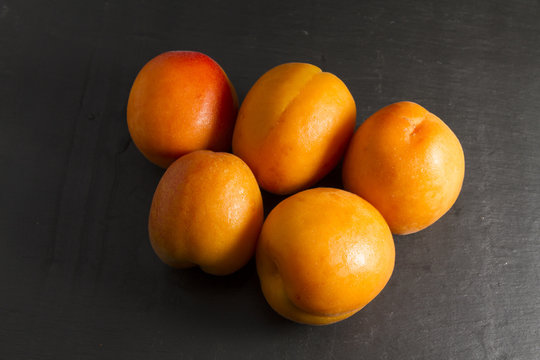 Five sun sweet apricots, one halved with stone. Prunus.