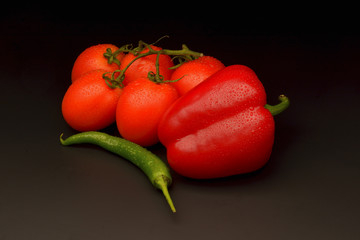 Tomatoes, sweet and chilli pepper on black background