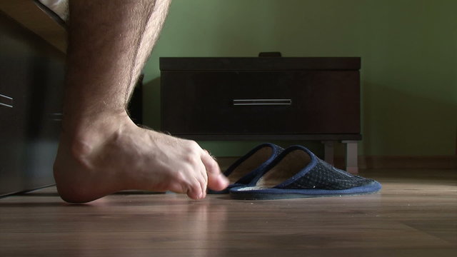 Male feet getting out of bed, put on slippers