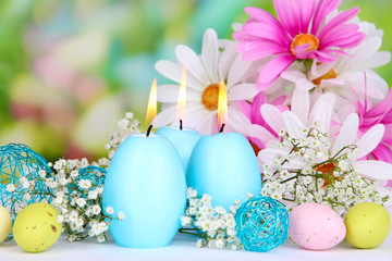 Easter candles with flowers on bright background