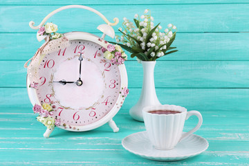Beautiful vintage alarm clock with flowers and cup of tea