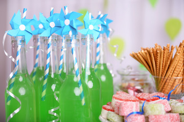 Bottles of drink with straw and sweets on decorative background