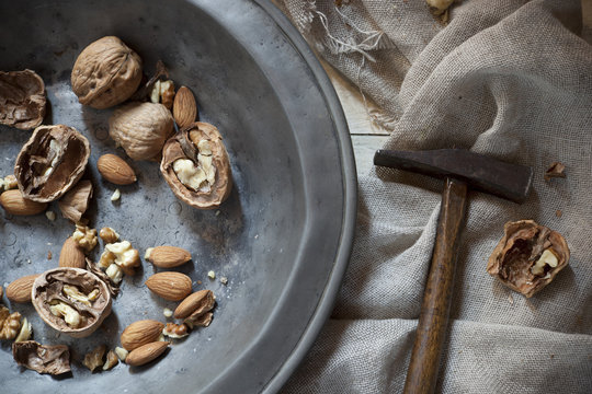 craked walnuts and whole almonds with hammer on vintage plate