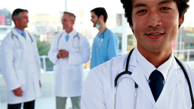 Doctor smiling at camera with team behind him