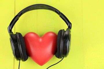 Headphones and heart on color wooden background