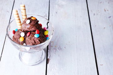 Chocolate ice cream with multicolor candies and wafer rolls in
