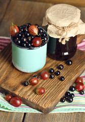 Ripe blackcurrants and gooseberries in mug and glass jar with