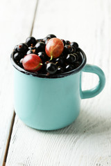 Ripe blackcurrants in mug on light wooden background.