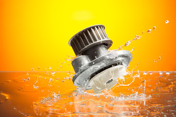 Auto parts, engine cooling pump in water splash on orange backgr