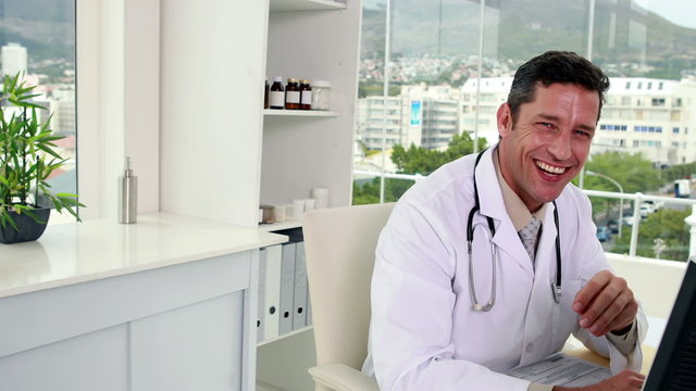 Handsome doctor working at his desk smiling at camera