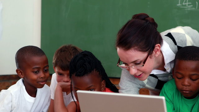 Pupils and teacher looking at laptop in classroom
