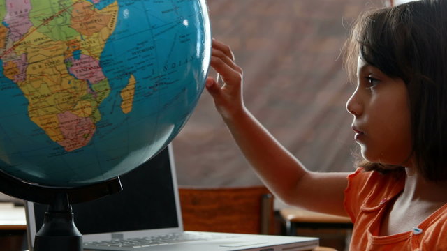 Little girl looking at globe in classroom