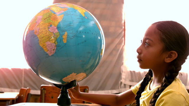Little girl looking at globe in classroom
