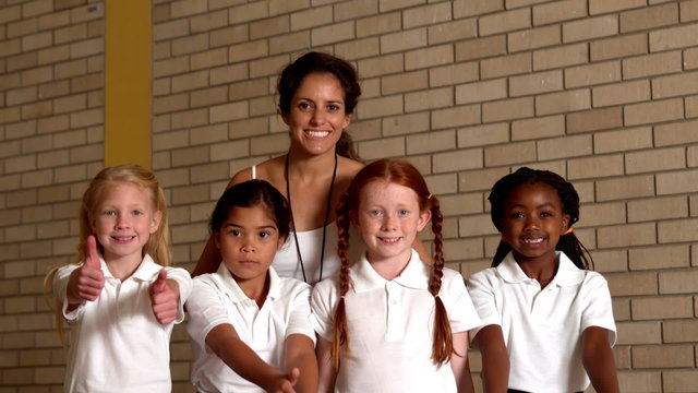 Cute pupils showing thumbs up with pe teacher