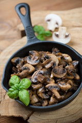 Frying pan with roasted champignons and green basil leaves