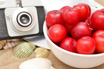 Red plums, old camera, shells and white hat on sand
