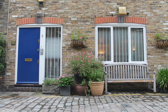A cosy porch with a blue door, a bench, flowers and two windows