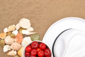 Plums, white hat and shells on wood and sand