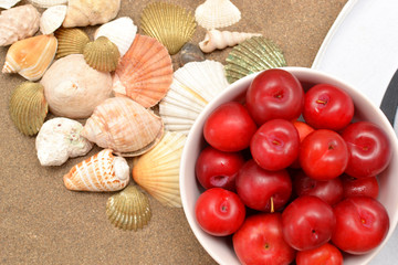 Plums, white hat and shells on wood and sand