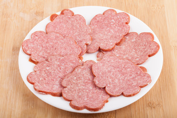 sliced ​​sausage on a white plate on wood