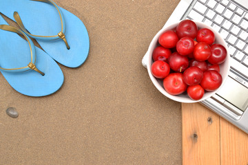 Slippers, laptop and plums on wood and sand