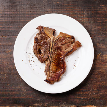 Grilled T-Bone Steak  on white plate on dark wooden background