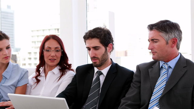 Business team sitting on couch having a meeting using laptop