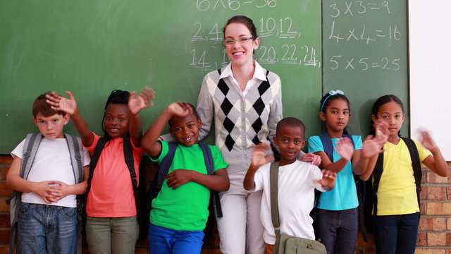 Pupils and teacher waving and smiling at camera in classroom