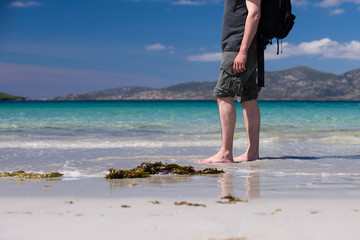 Male taking a walk on a white sandy beach with turquoise water