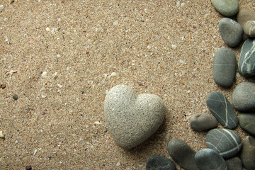 Fototapeta na wymiar Grey stone in shape of heart, on sand background