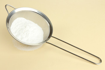Powdered sugar in metal sieve on beige background