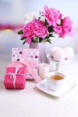 Composition of beautiful peonies in vase, tea in cup and