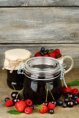 Tasty jam with berries in glass jars on wooden table