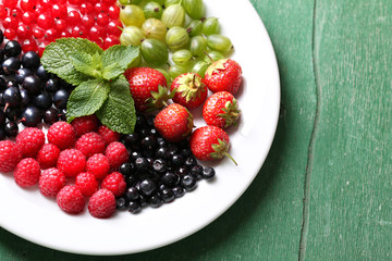 Forest berries on plate, on color wooden background