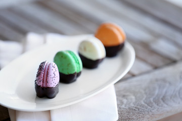 Colorful macaroons in plate on wooden table, close-up