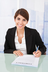 Smiling Businesswoman Signing Contract At Desk