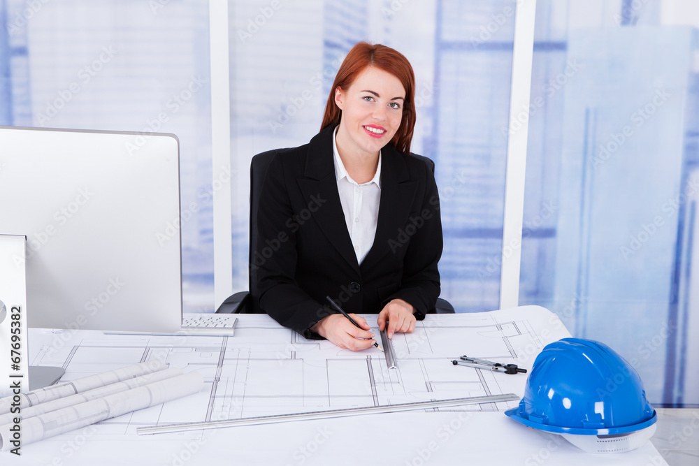 Poster businesswoman using computer with blueprints at desk
