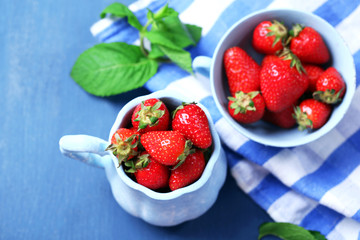 Ripe sweet strawberries in mugs  on color wooden background