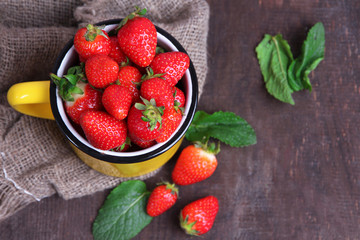 Ripe sweet strawberries in mug  on color wooden background