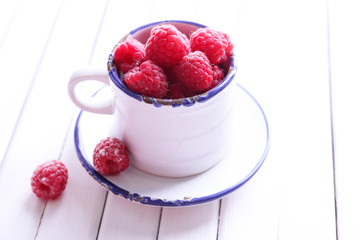 Ripe sweet raspberries in cup on table close-up