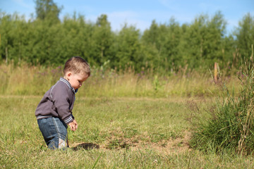 Naklejka na ściany i meble Little boy stands at green meadow and looks down in summer