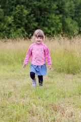 Little beautiful girl in skirt goes at green meadow in summer