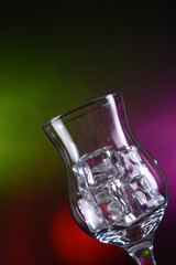 Glass with ice cubes on color background