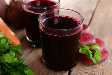 Glasses of fresh beet juice and vegetables on wooden background